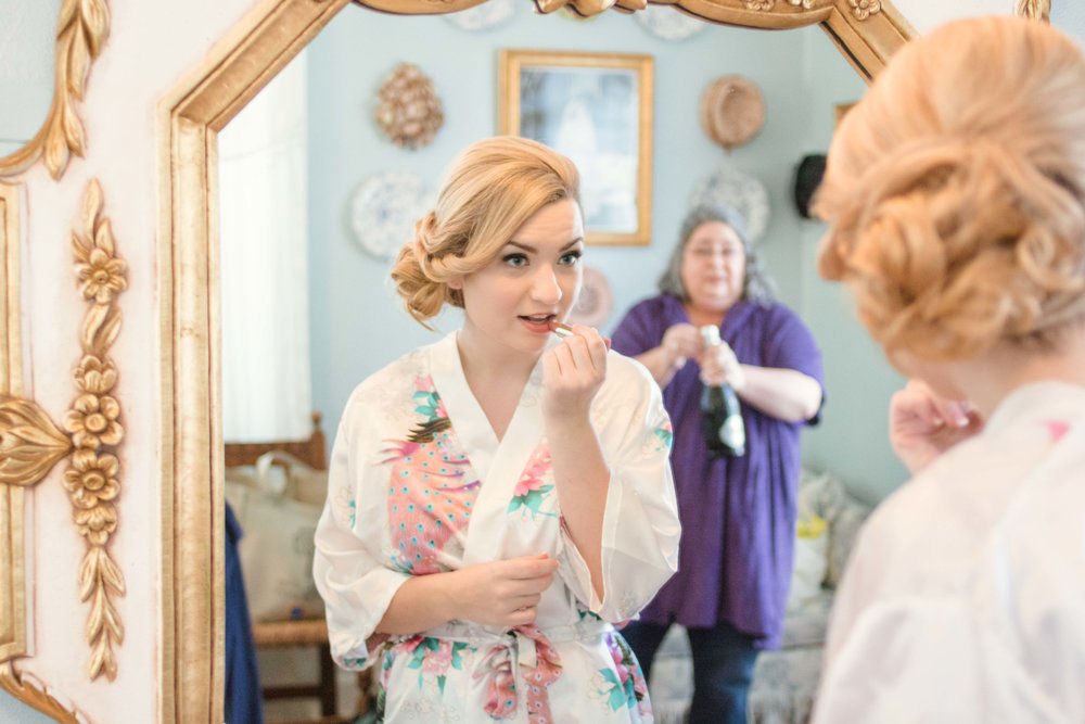 A bride puts on lipstick in front of the ornate mirror at the Gassaway Mansion Bride's Room