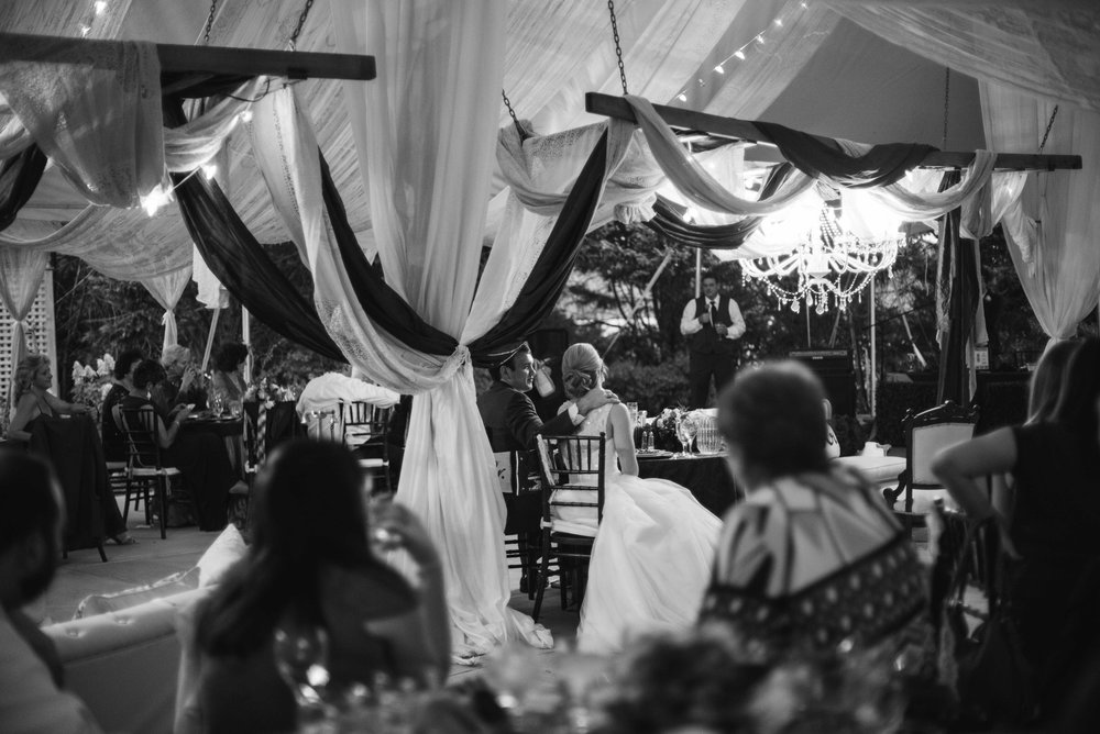 reception at the gassaway mansion. This black and white image shows the couple sitting during the toasts looking at each other. The drapery hanging all over the tent frames the couple in the middle.