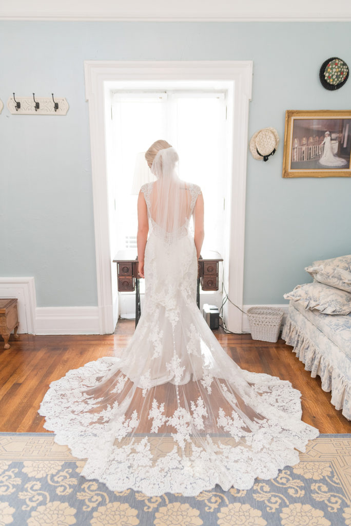 The bride's room at the gassaway mansion. The walls are light blue and there are old wood floors. The bride is facing the window and the image showcases her lacy train.