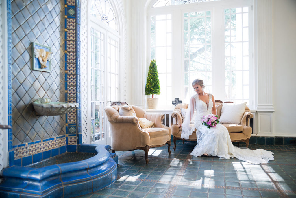 Bridal portraits on a vintage style couch in a room with blue tyle, a fountain, white walls, and large windows at the Gassaway Mansion