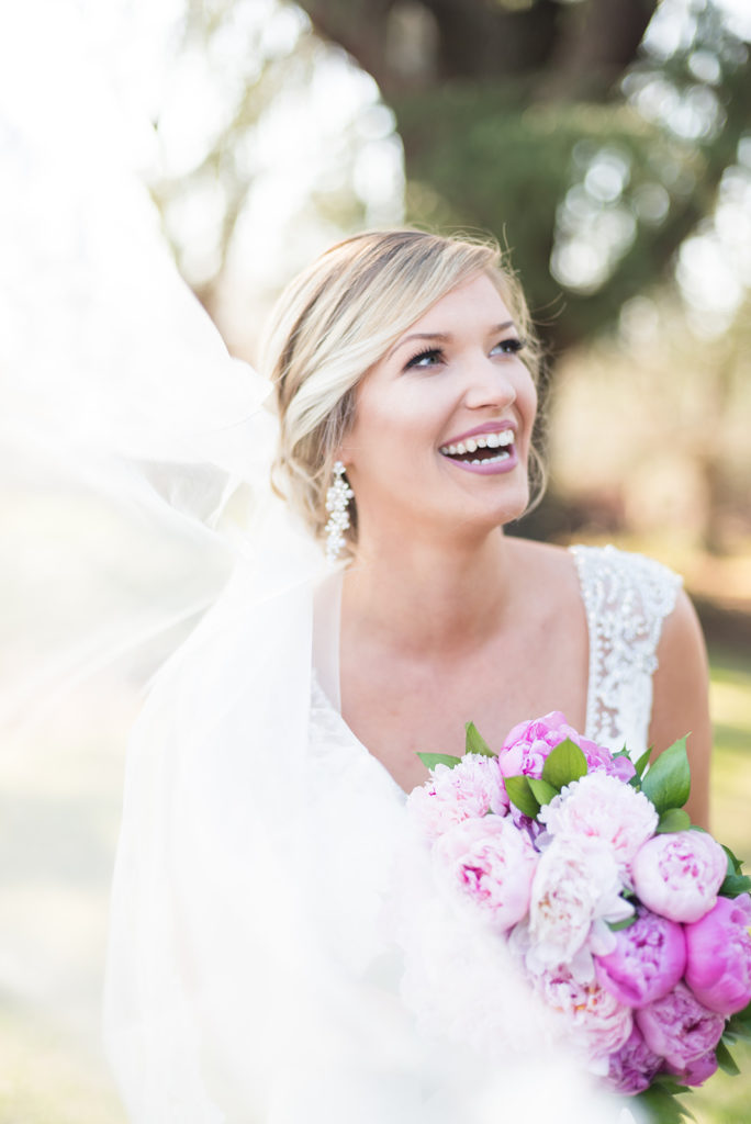 Joyful bridal portraits at the gassaway mansion. The bride is smiling to the right and her veil is flying in the wind. You can see her pink peonies in the foreground.