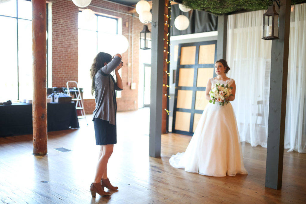 Christi is photographing a bride in a venue with exposed brick and columns. There are fairy lights on the columns and light coming in from the windows. Greenville Wedding Photographers ready to serve you!