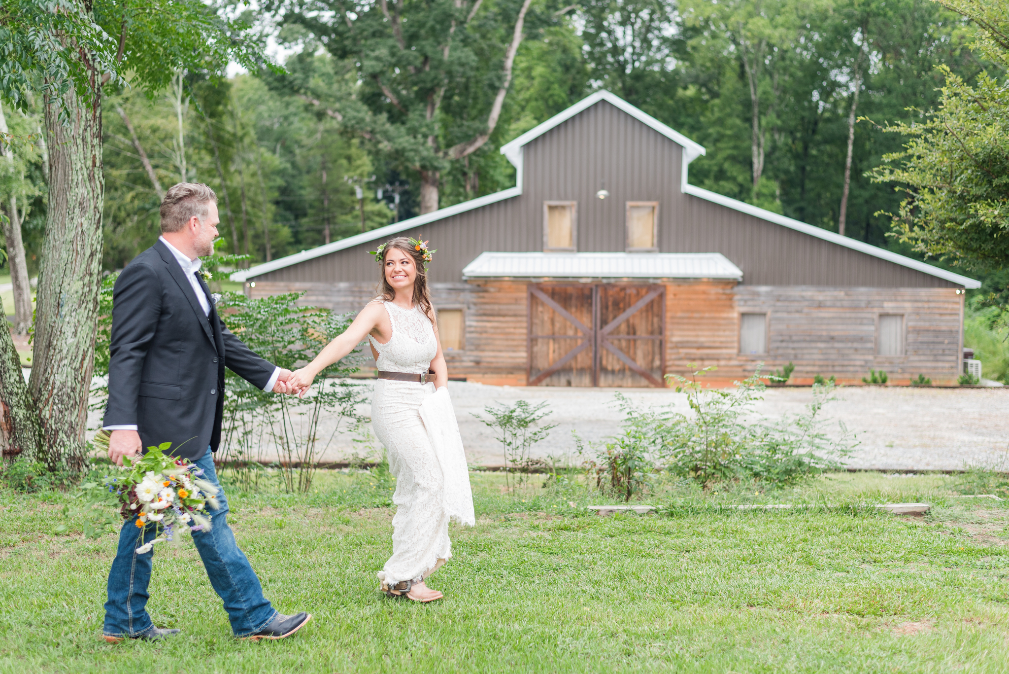 A bride and groom are walking in front of Iron Oak Barn - a rustic barn clad in brown