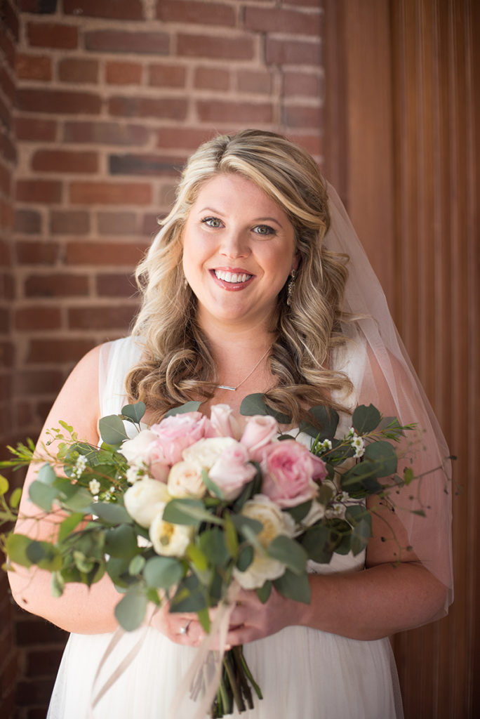 A bride on her wedding day in front of exposed brick at The Upper Room in Greenville, SC