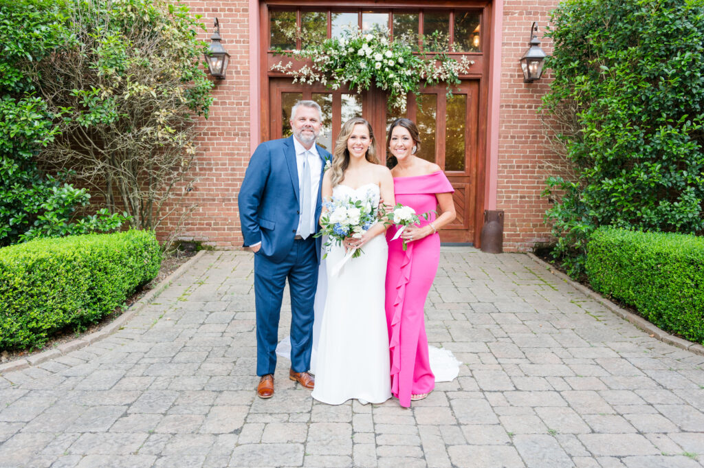 A bride with her dad in a navy suit and her stepmom in a beautiful pink dress at the bleckley inn