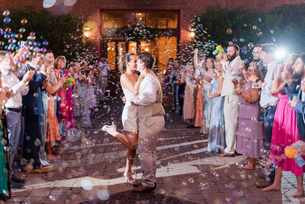 A bride and groom share a kiss with guests blowing bubbles as they exit their wedding at the bleckley inn