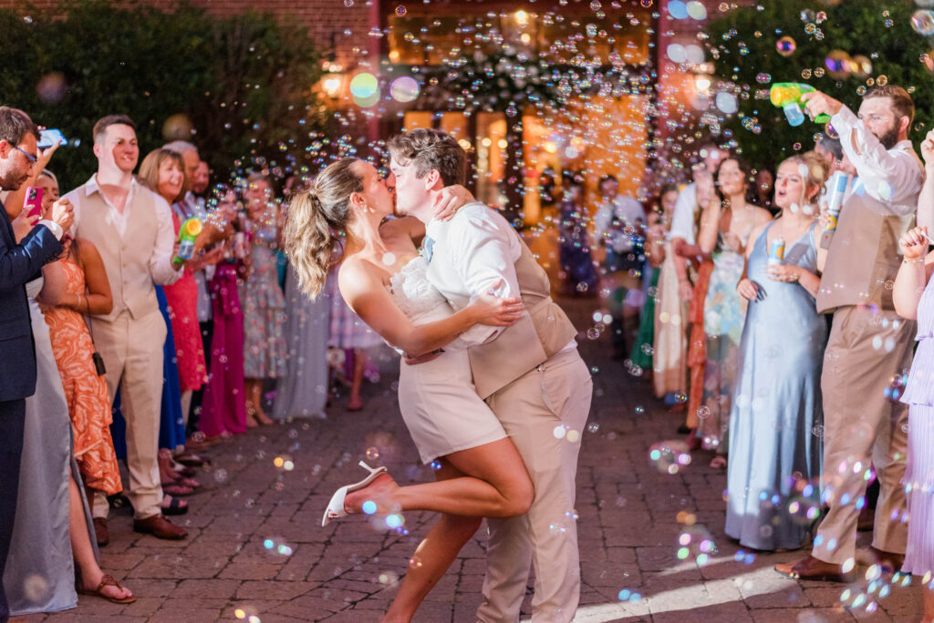 A bride and groom share a kiss with guests blowing bubbles as they exit their wedding at the bleckley inn