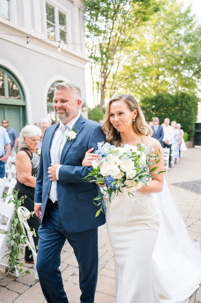 A bride walks down the aisle escorted by her father at the carriage house at the bleckley inn