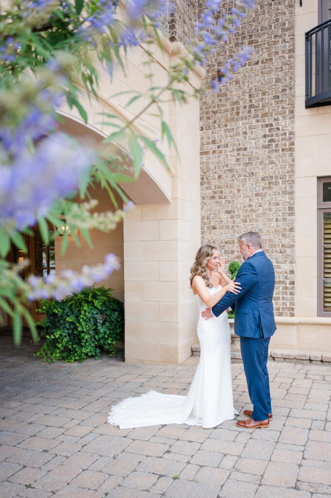 A bride and her father share a sweet and teary moment during their first look at a wedding at The Bleckley Inn with purple flowers in the foreground