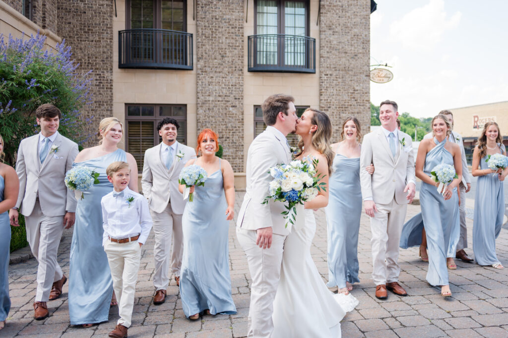 A wedding party walking towards the camera while a bride & groom embrace and share a kiss in front of the bleckley inn in anderson sc